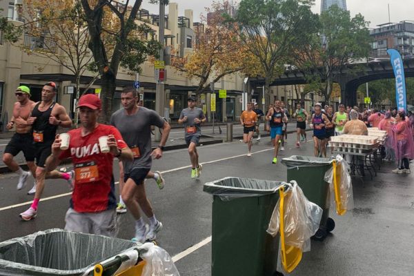 Marathon runners disposing paper cups in bins after drinking from them.